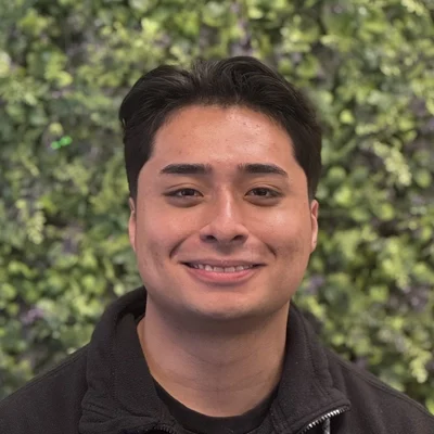 Jose Flores smiling in front of greenery.